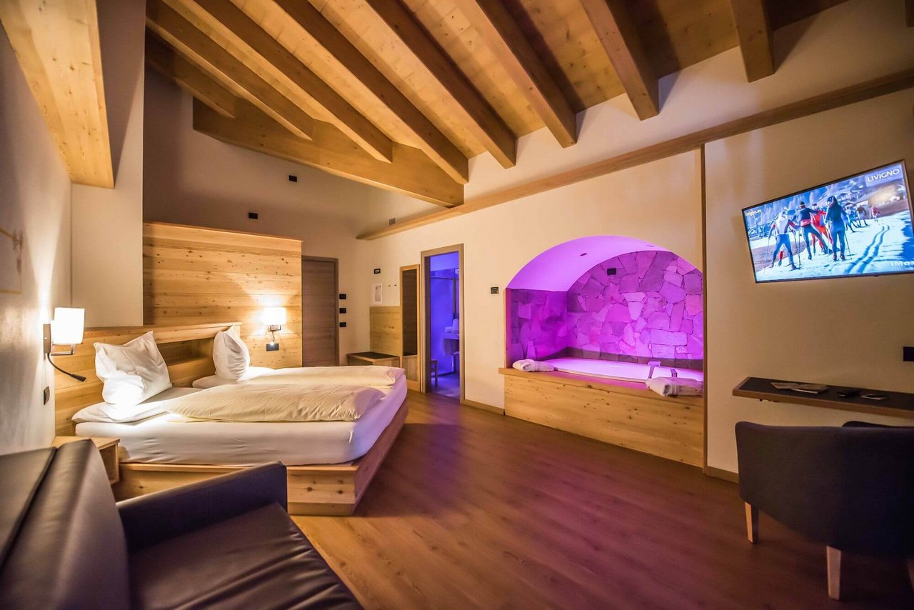 Stessa camera in legno con vasca idromassaggio illuminata e letto matrimoniale, inquadratura identica