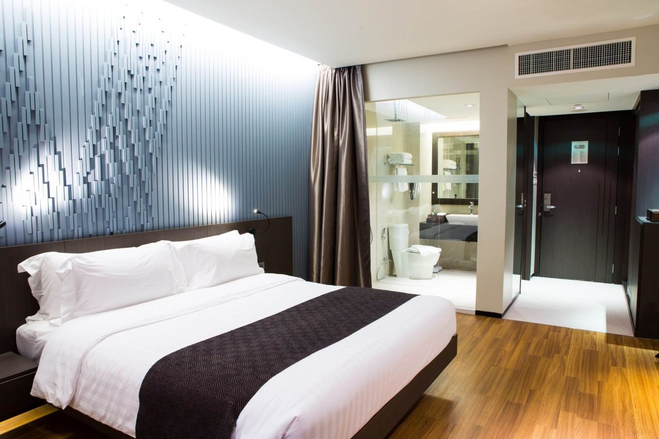 Camera moderna con letto matrimoniale, parete decorativa a listelli, bagno con vetrata e porta d'ingresso