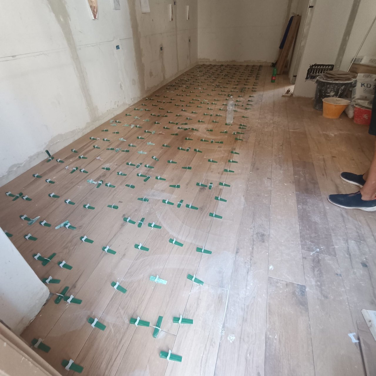 Ampio locale in cantiere con piastrelle appena posate, distanziatori verdi, secchi e piede di un operaio