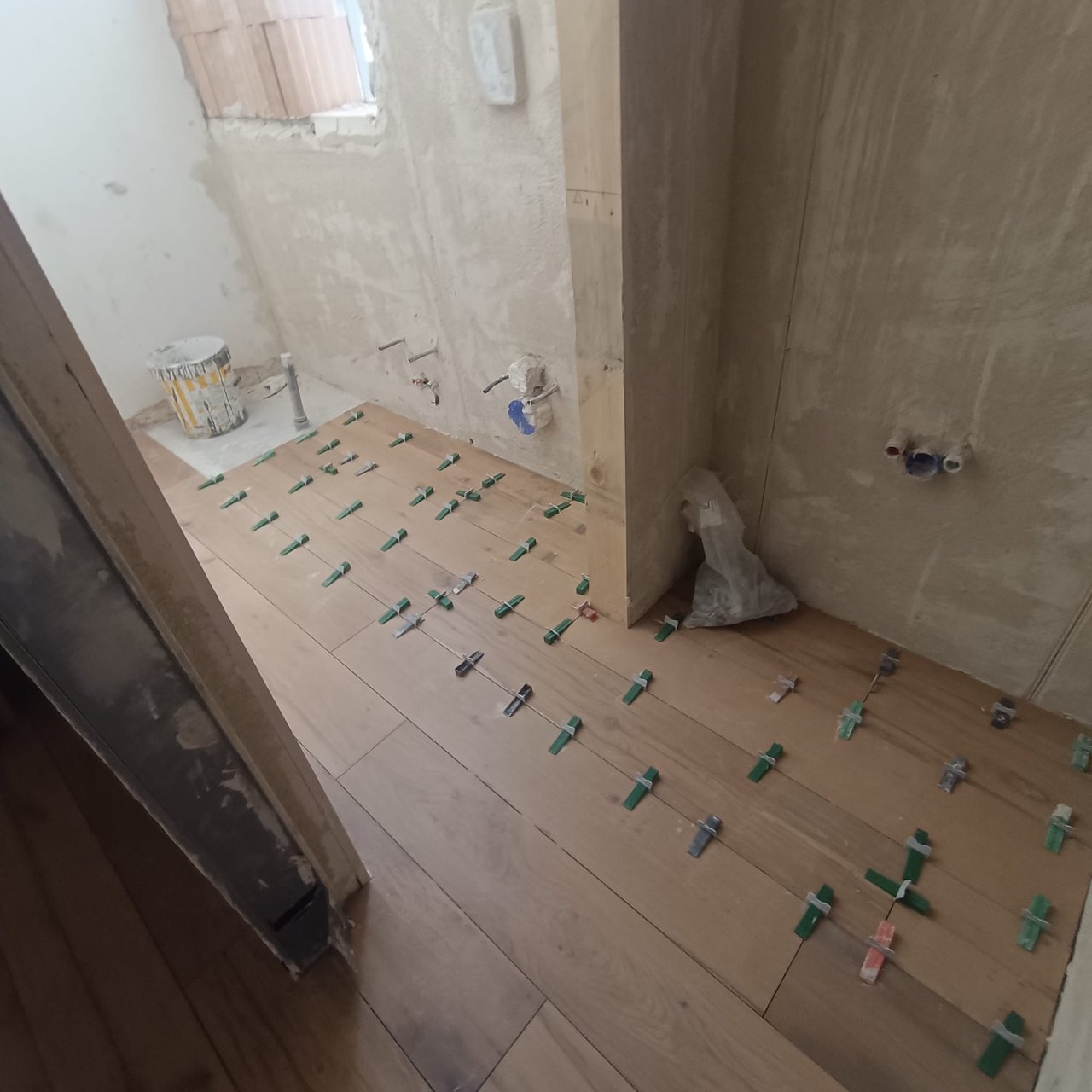Piccolo vano in cantiere con pavimento in posa, tubi idraulici a muro e sacchetti di materiale