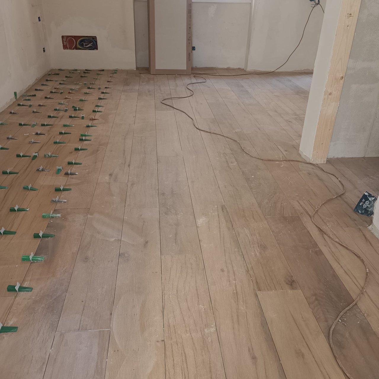 Stanza in cantiere con posa di piastrelle effetto legno, distanziatori, cavi elettrici a terra
