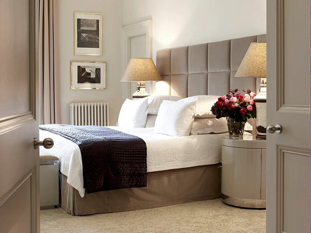 Camera con letto matrimoniale, lampade abat-jour e mazzo di rose sul comodino tondo, identica alle precedenti