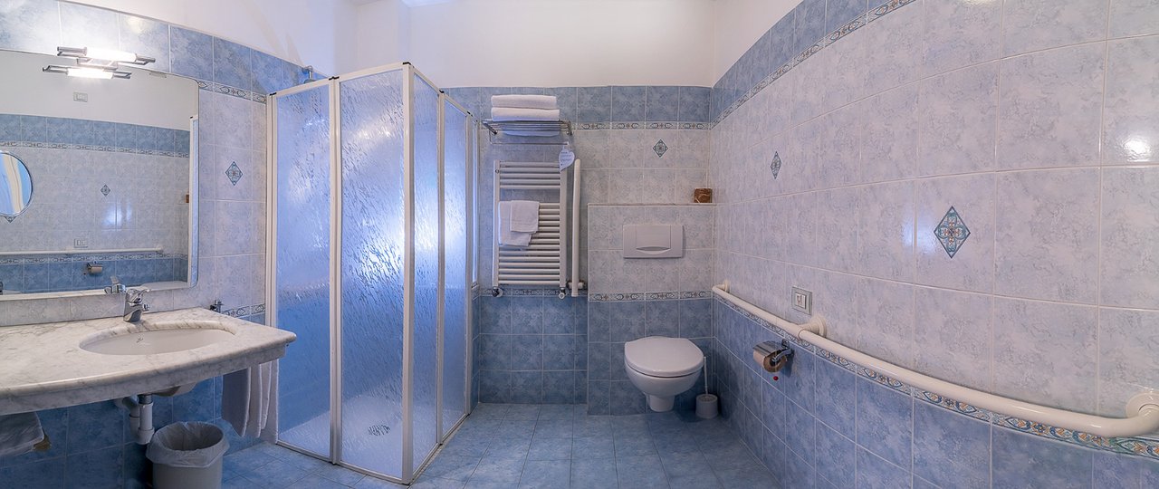 Bagno azzurro con lavabo in marmo, box doccia e wc, ripresa panoramica identica alle altre