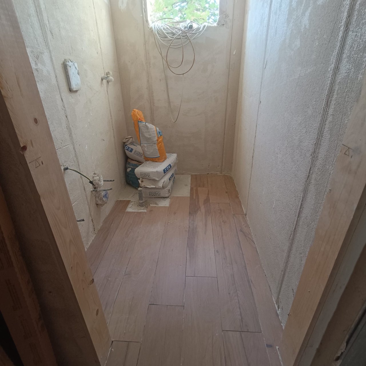 Corridoio o vano stretto grezzo con sacchi di cemento, matassa di cavo e pavimento parzialmente posato